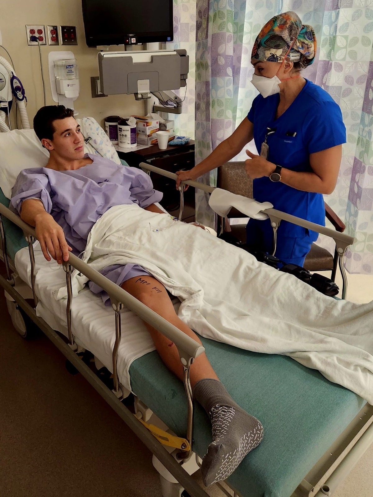 Nico in a hospital bed after knee surgery speaking with a nurse